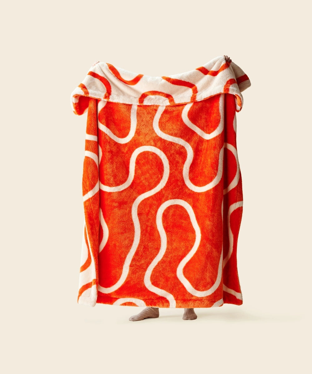 Plaid wavy orange polaire waro tendu par une personne sur un fond beige