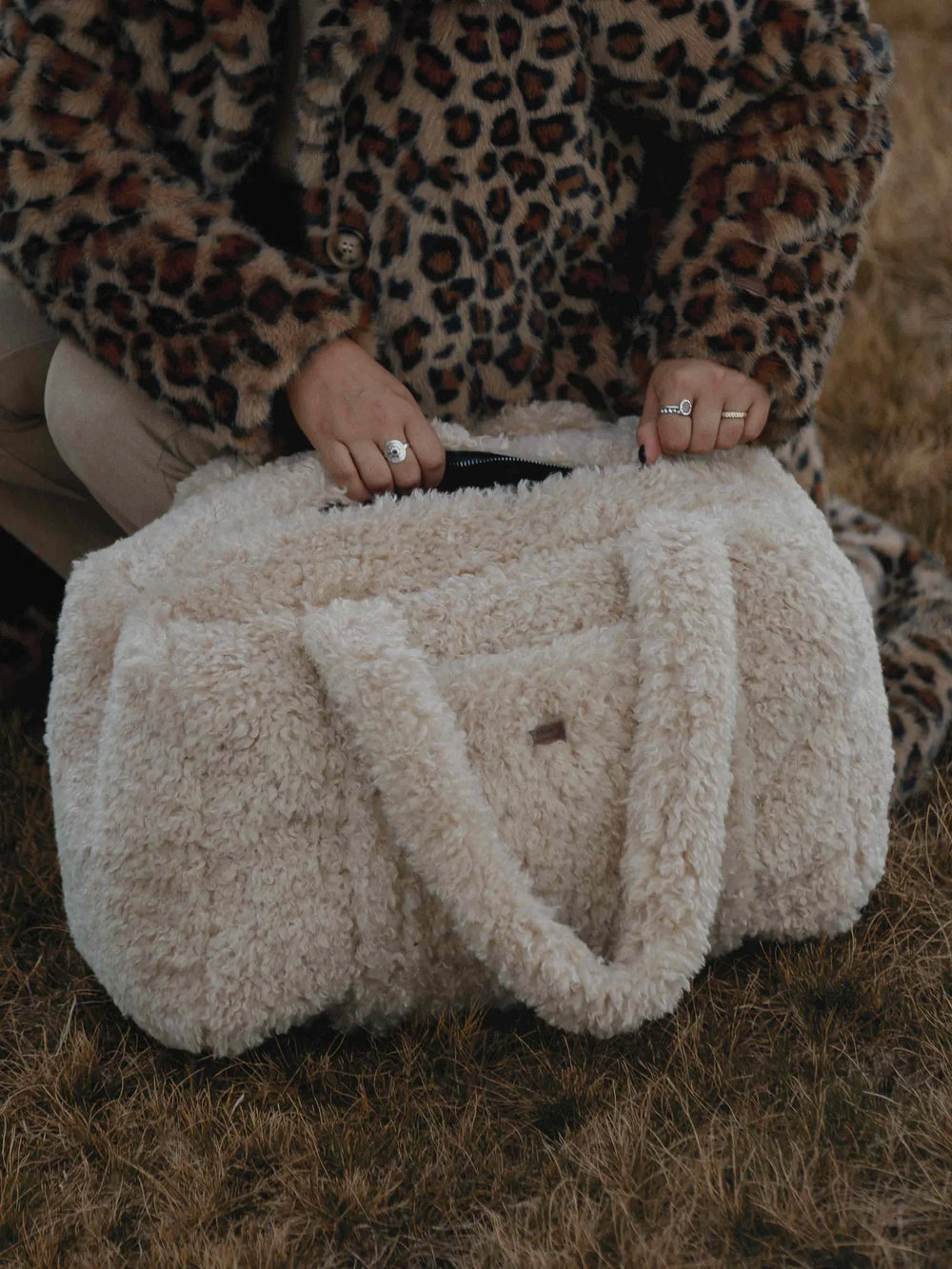 Sac weekender en bouclette beige waro tenu à deux mains par une femme portant un manteau à motif animal.