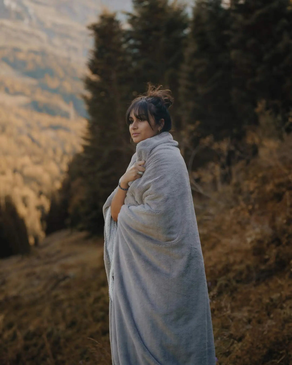 Cosy two-tone frosted WARO blanket in light grey worn by a woman in the mountains, a warm, wintry ambience