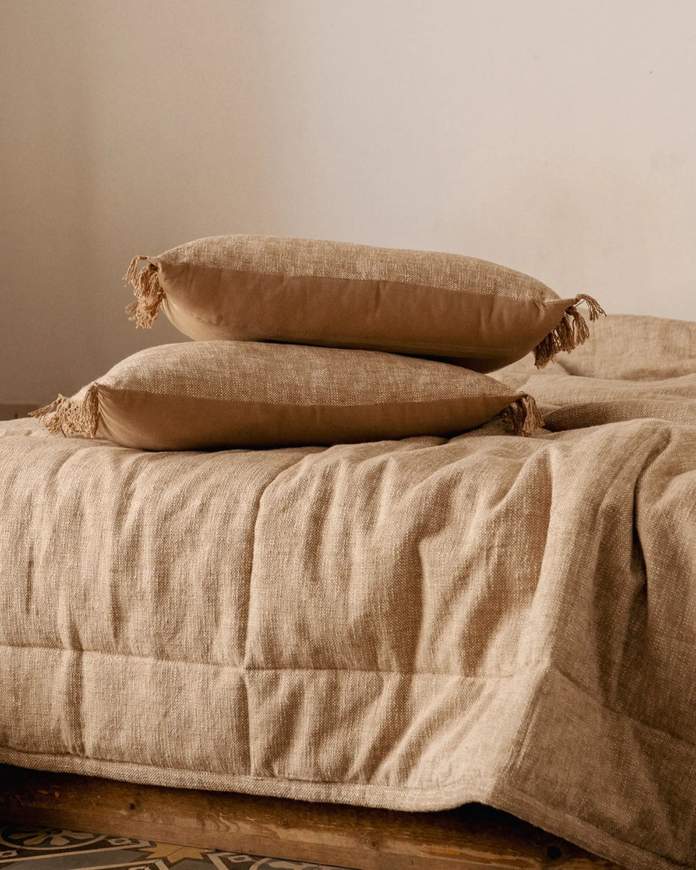 Coussin en coton beige WARO sur un lit, ambiance naturelle et chaleureuse
