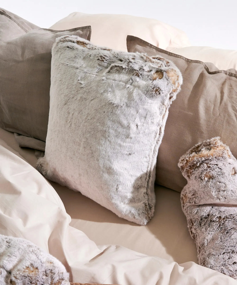 Coussin fausse fourrure Frisson Naturel waro posé sur un lit