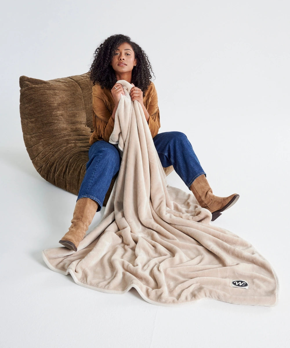 Plaid polaire waro beige waro tenu par une femme assise sur un togo taupe
