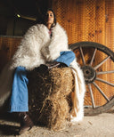 Plaid fausse fourrure douchka entrelacé autour d’une femme assise sur une botte de foin