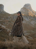 Femme portant un manteau en fausse fourrure léopard en extérieur, paysage montagneux en arrière-plan.