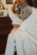 Seated person wrapped in the WARO Maxi Berber Plaid in a relaxing atmosphere
