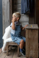 Enfant assis sur une chaise avec le Plaid Polaire Bébé Berbère WARO derrière lui