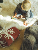 Enfant jouant sur un plaid cocoon rouge à motifs flocons, plaid chaud et doux WARO pour l’hiver et les moments cocooning
