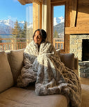 Plaid fausse fourrure marron waro enroulé autours d’une femme assise sur un canapé