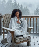 Plaid polaire cerf gris waro enroulé autours d’une femme assise sur une chaise