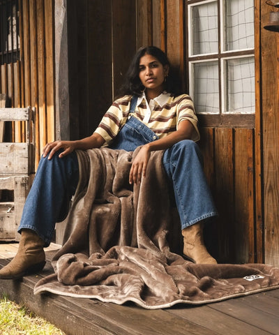 Plaid polaire waro taupe posé sur une femme assise dans un ranch 
