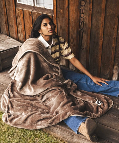 Plaid polaire waro taupe posé su une femme assise au sol dans un ranch