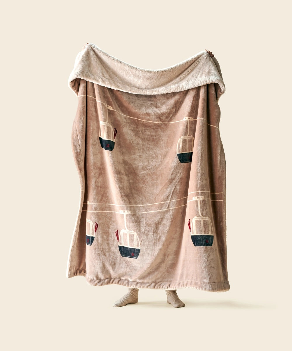 Plaid telecabine beige waro polaire tendu par une personne sur un fond beige 