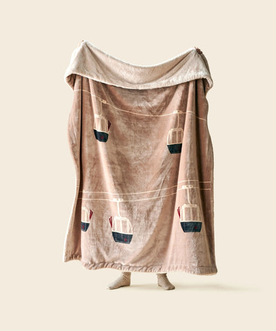 Plaid telecabine beige waro polaire tendu par une personne sur un fond beige 