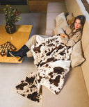 Plaid polaire motif vache porté sur un canapé, style cosy et décoratif