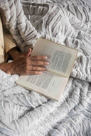 Plaid polaire tigre beige waro mit sur un lit avec au dessus une femme feuillant un livre