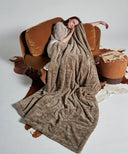 Plaid polaire tigre taupe waro posé sur une femme assise sur un canapé marron