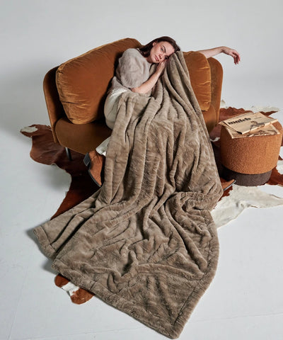 Waro taupe tiger fleece blanket over a woman sitting on a brown sofa