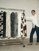 Femme présentant une collection de plaids WARO en fausse fourrure suspendus sur un portant, dans un univers intérieur épuré