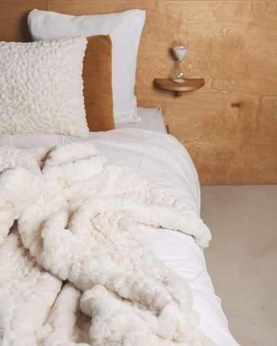 Couvre-lit en fausse fourrure galet waro disposé sur un lit blanc