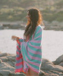 Fouta Solenza bleu portée sur les épaules face à la mer, fouta rayée en coton doux et absorbant