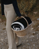 Plaid cosy bicolore noir et gris WARO transporté dans un panier en osier en pleine nature