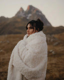 Femme portant un plaid fausse fourrure galet blanc avec sangles en cuir vegan lors d’une balade en extérieur.