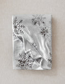plaid polaire gris clair motif flocon de neige posé a plat sur un fond beige 