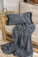 Coussin en coton indigo WARO posé sur un canapé, finition frangée naturelle