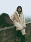Manteau Teddy Bear beige WARO en fausse fourrure porté lors d’un shooting avec un cheval dans un environnement naturel.